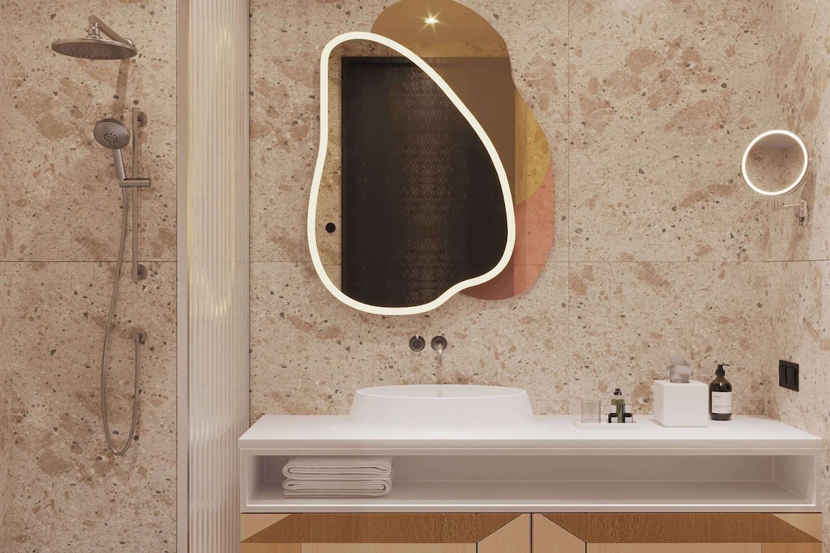 A modern bathroom with a freestanding shower, a large mirror with a light, and a white sink with a towel rack.