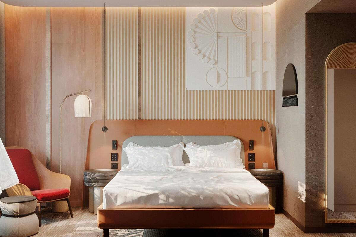 A modern hotel room with a large bed, a red armchair, a small round table, and a wall-mounted light fixture.