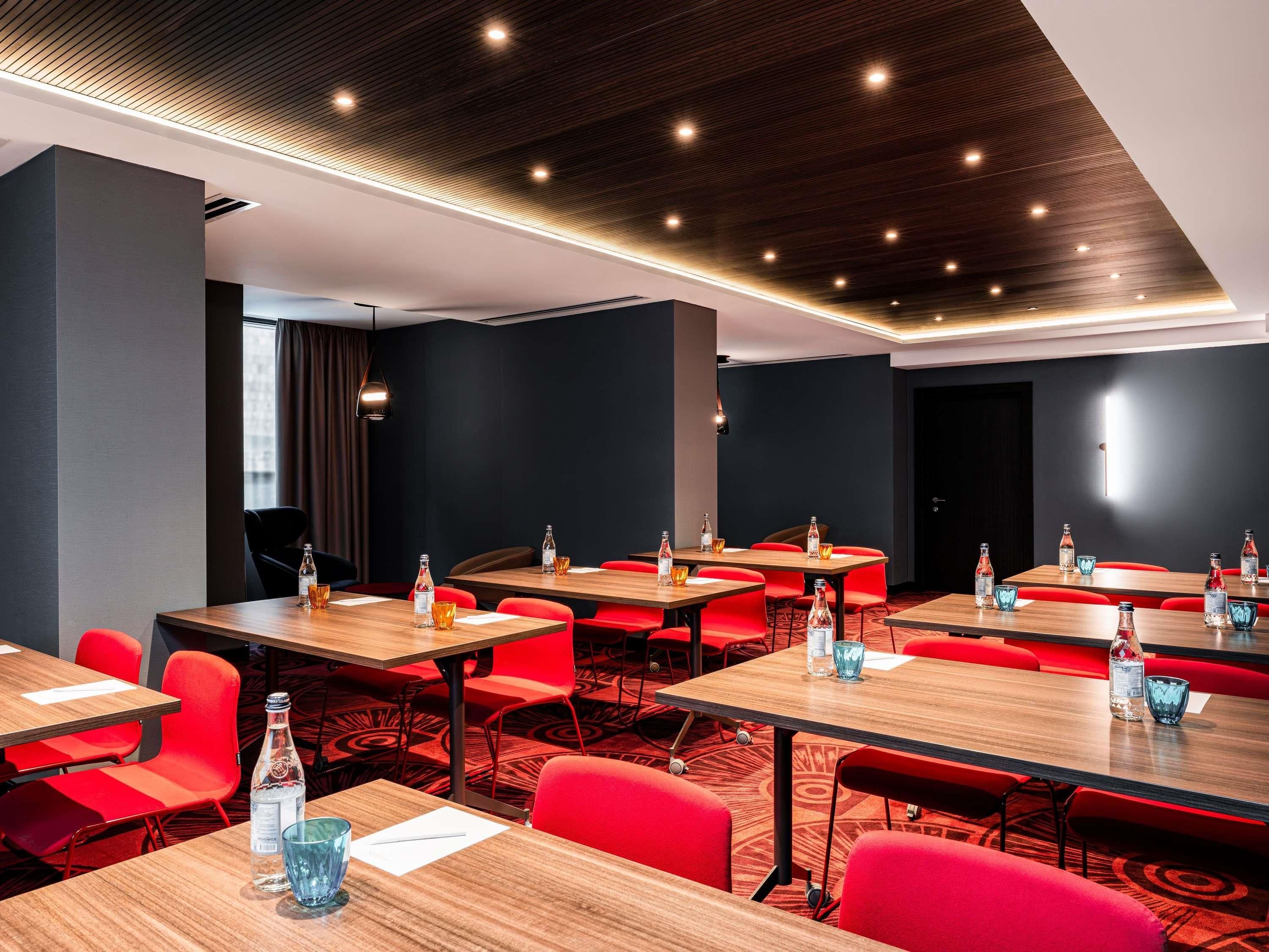 A conference room with multiple tables and red chairs, equipped with water bottles and glasses.