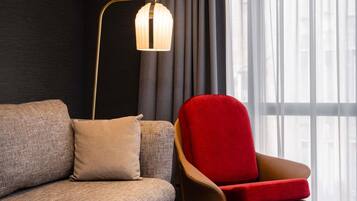 A modern living room with a sofa, a red armchair, a floor lamp, and a window with sheer curtains.
