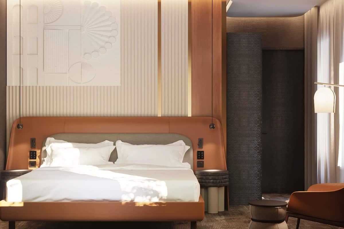 A modern hotel room with a large bed, bedside tables, a chair, and a unique wall design.