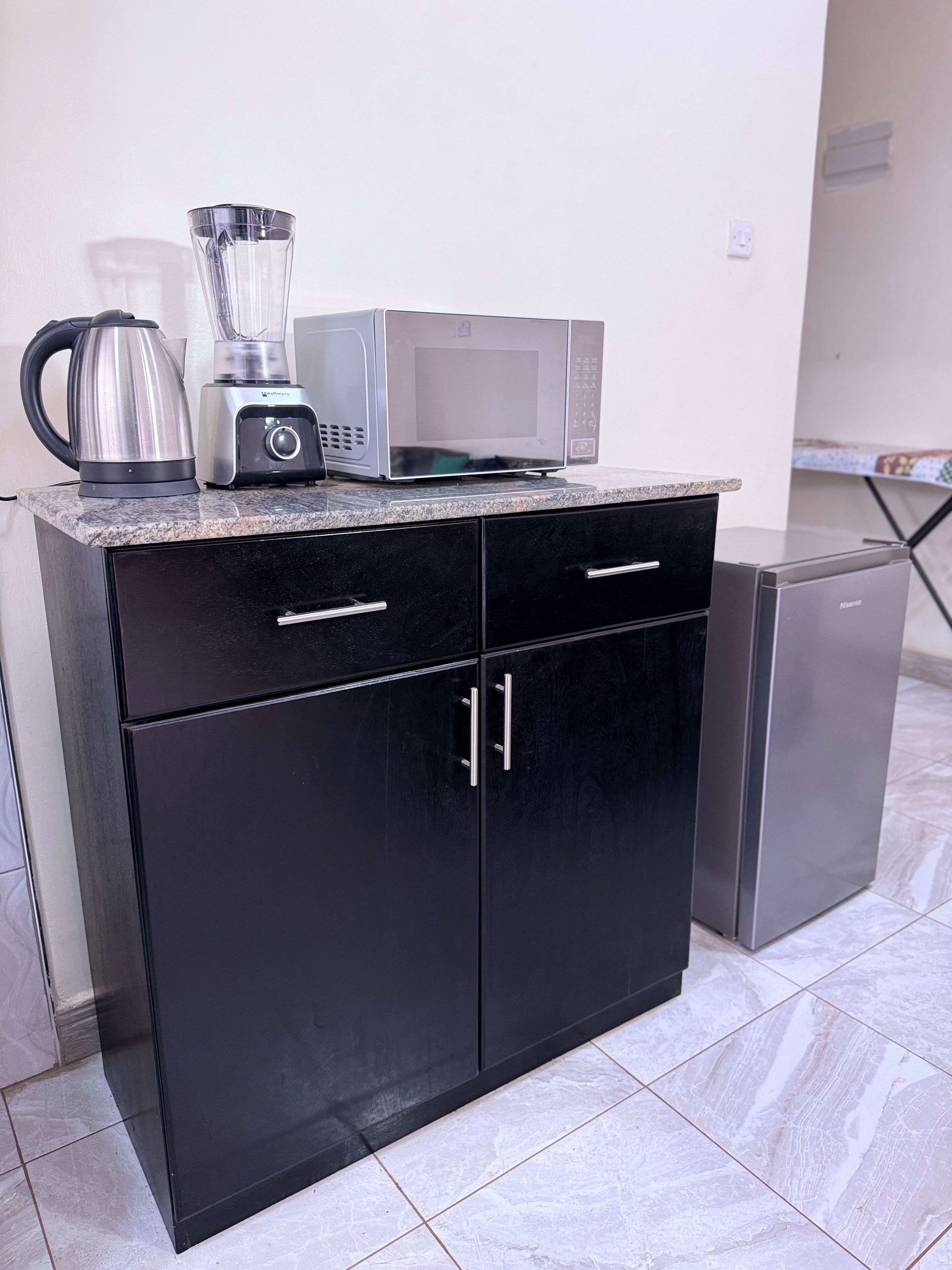 A kitchen with a black cabinet, a coffee maker, a blender, and a microwave.
