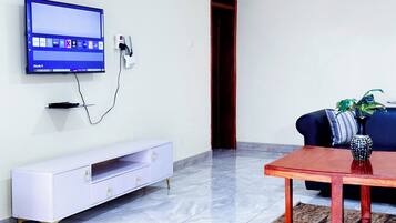 A living room with a flat-screen TV mounted on the wall, a white entertainment unit, a wooden coffee table, and a blue sofa with a plant.