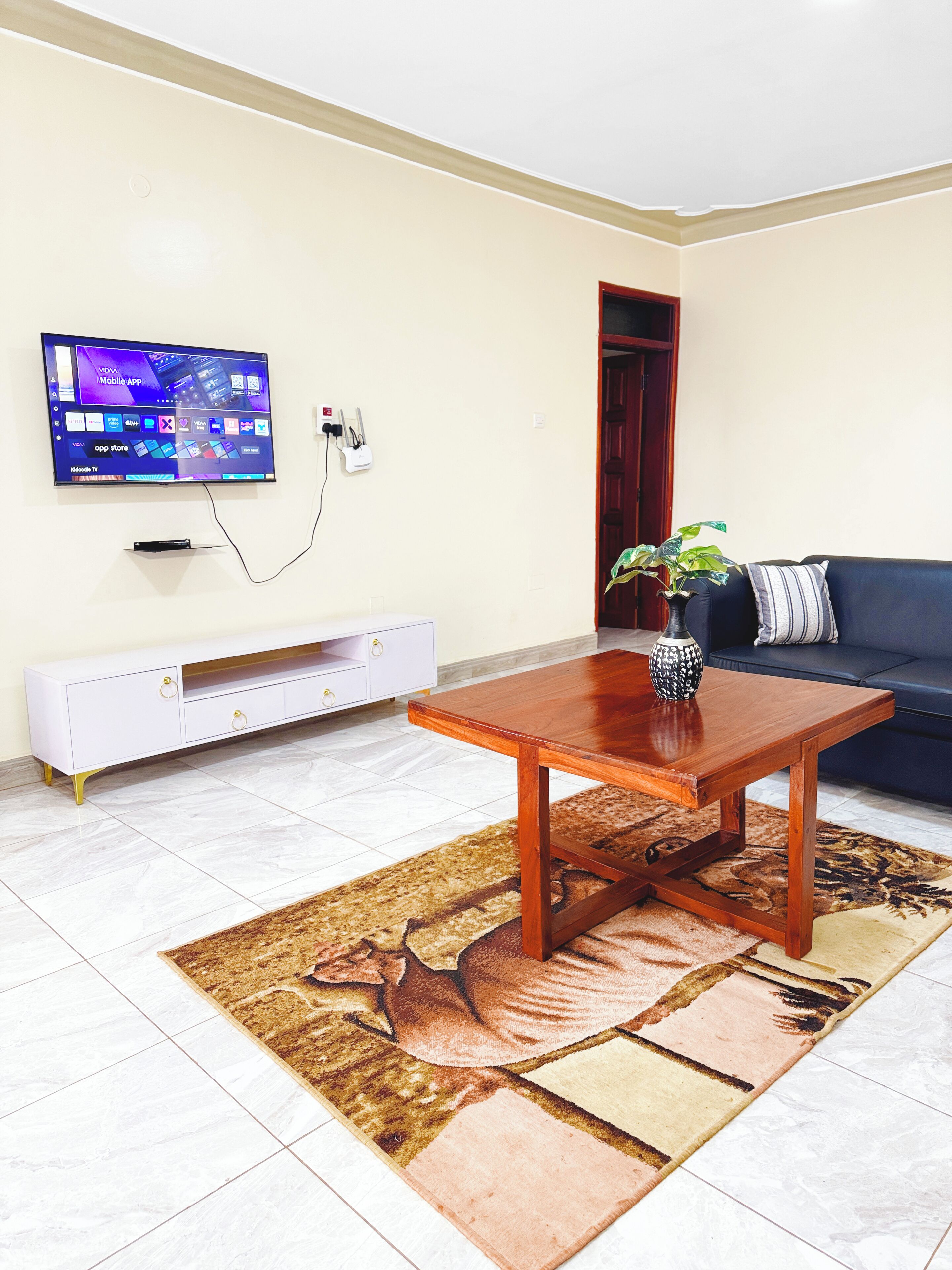 A living room with a flat-screen TV mounted on the wall, a wooden coffee table, a sofa, a patterned rug, and a white entertainment unit.