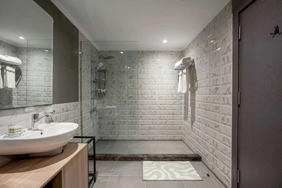 A modern bathroom with a glass shower enclosure, a marble-tiled shower area, and a wooden vanity with a sink.