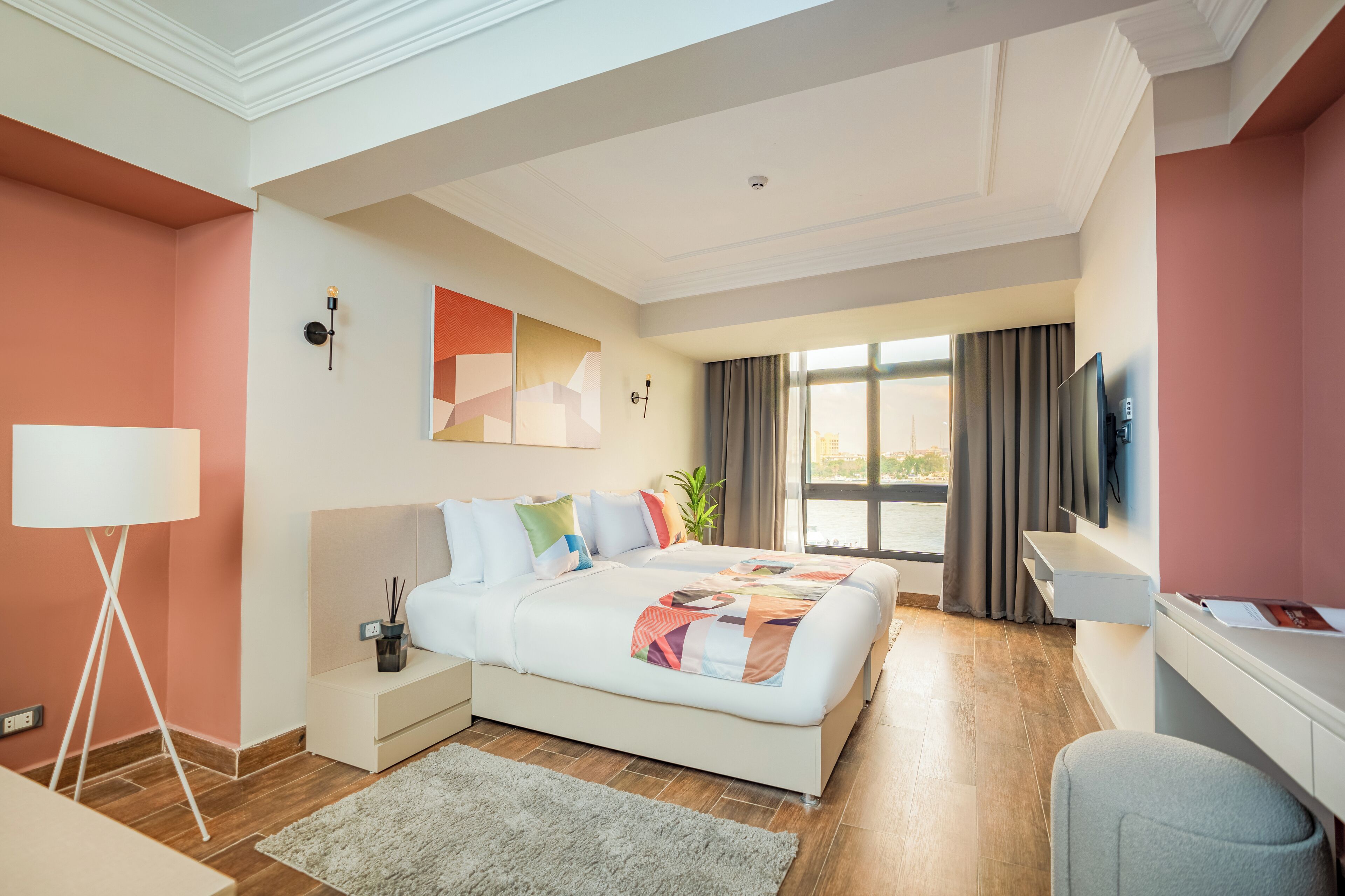 Una habitación de hotel moderna con una cama grande, un escritorio, un televisor y vistas al exterior.
