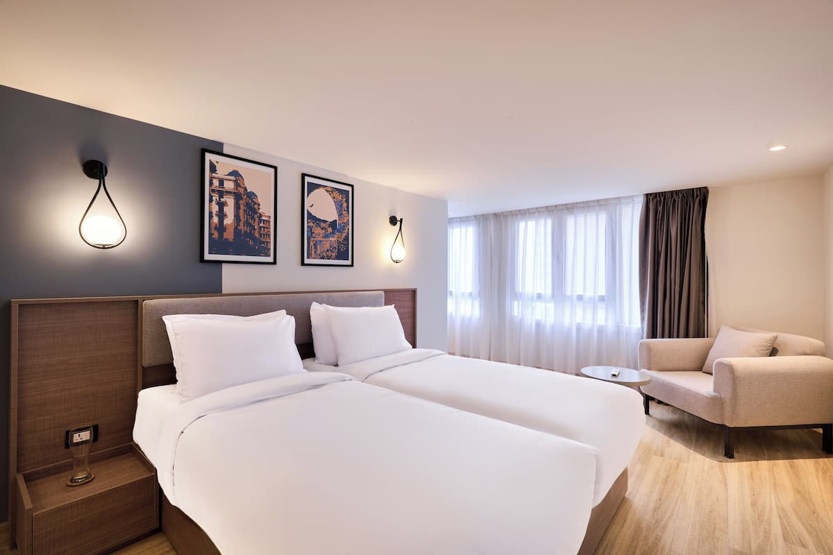 Une chambre d’hôtel avec deux lits, un canapé, une petite table et des œuvres d’art accrochées au mur.