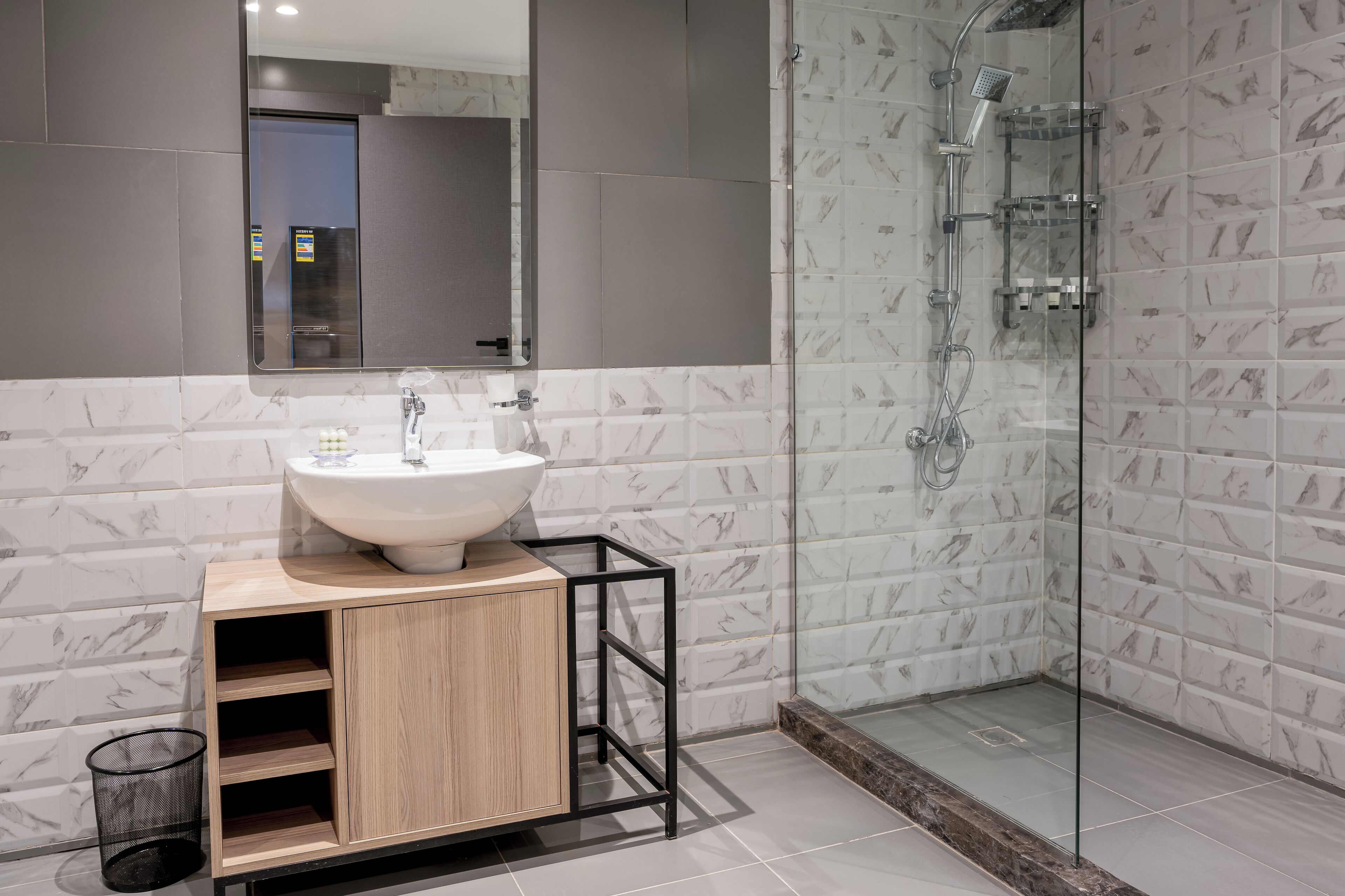A modern bathroom with a marble-tiled shower, a wooden vanity with a sink, and a large mirror.