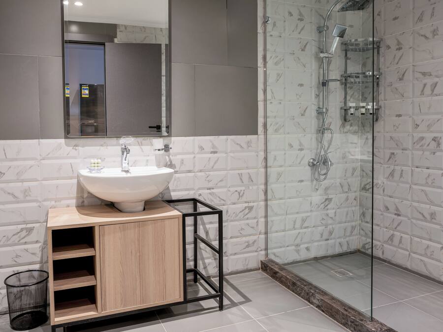 A modern bathroom with a marble-tiled shower, a wooden vanity with a sink, and a large mirror.