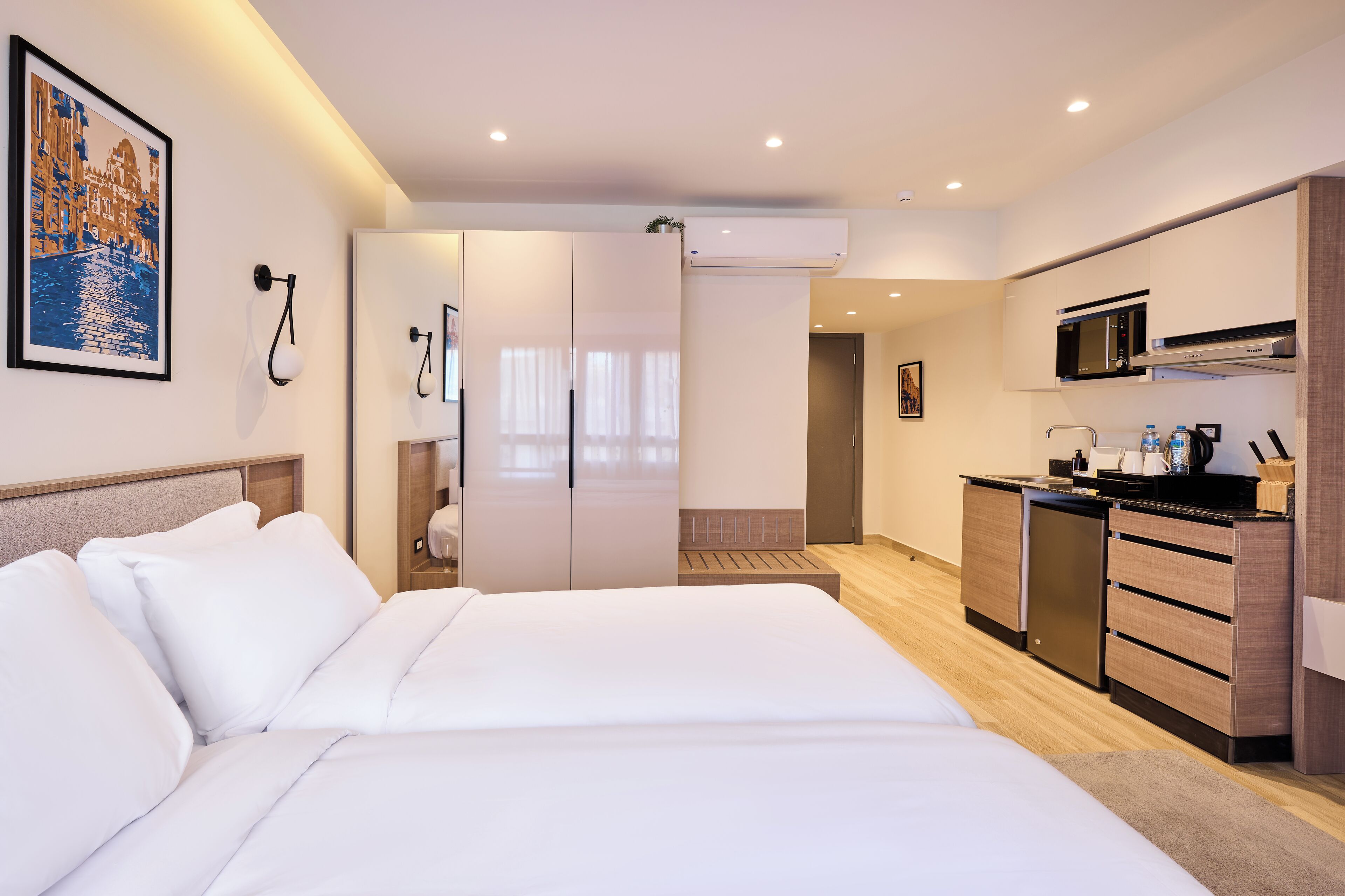 A modern hotel room with a large bed, a kitchenette, and a bathroom with a shower and toilet.