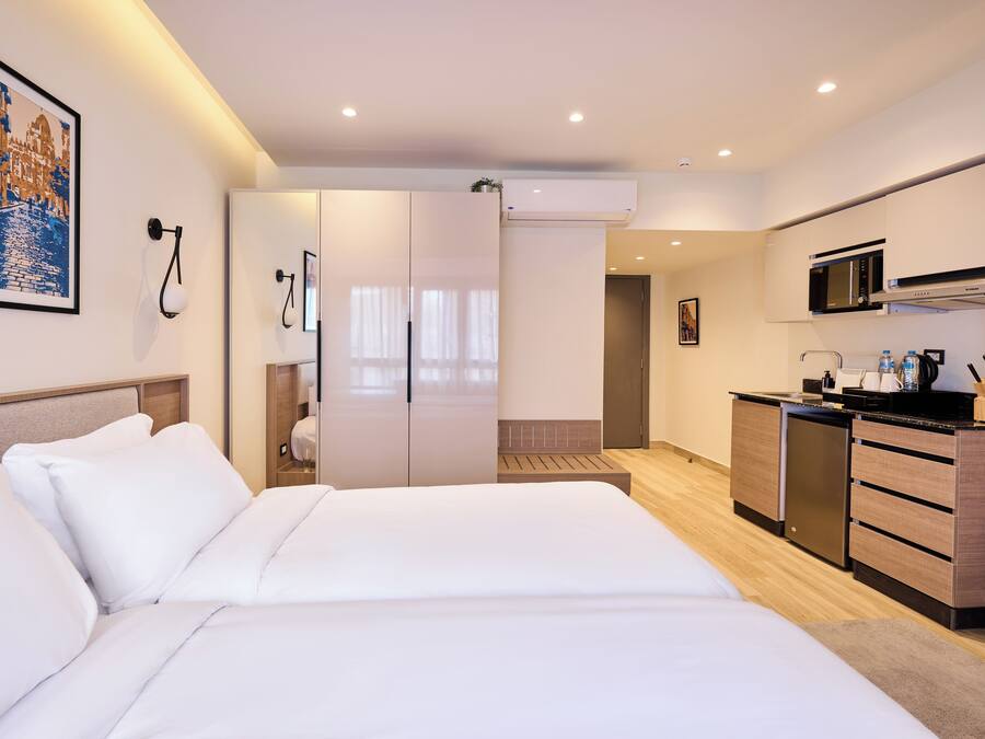 A modern hotel room with a large bed, a kitchenette, and a bathroom with a shower and toilet.