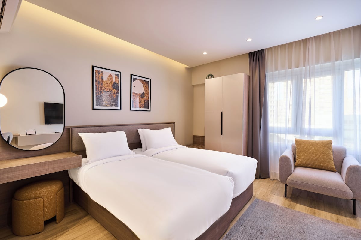 Une chambre d’hôtel avec un lit double, un bureau avec une chaise, une armoire et une grande fenêtre avec des rideaux.