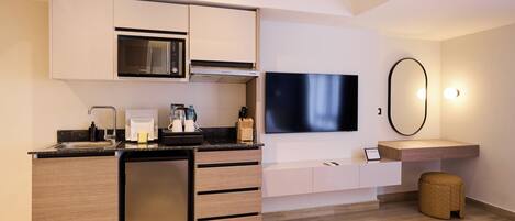 Una habitación de hotel moderna con kitchenette, televisor de pantalla plana, una pequeña zona de estar y un espejo grande.