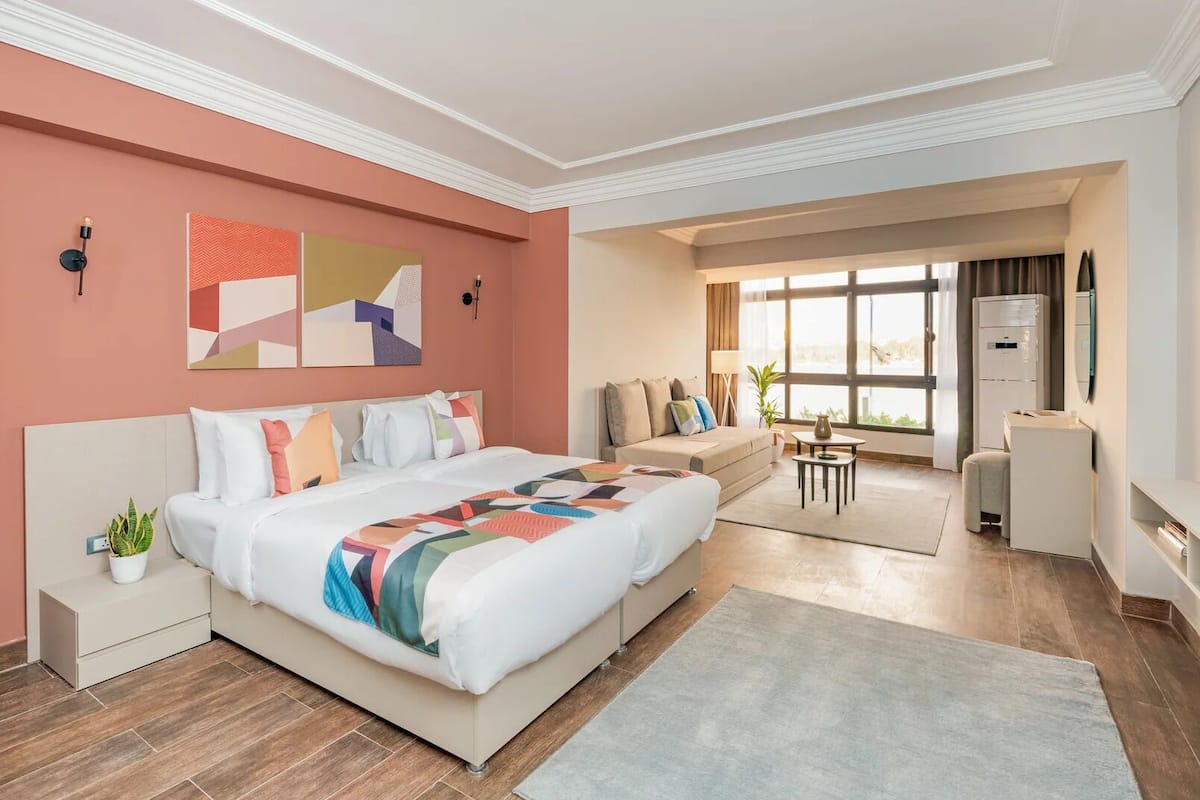 Une chambre d’hôtel moderne avec un grand lit, un canapé, une petite table et un réfrigérateur.
