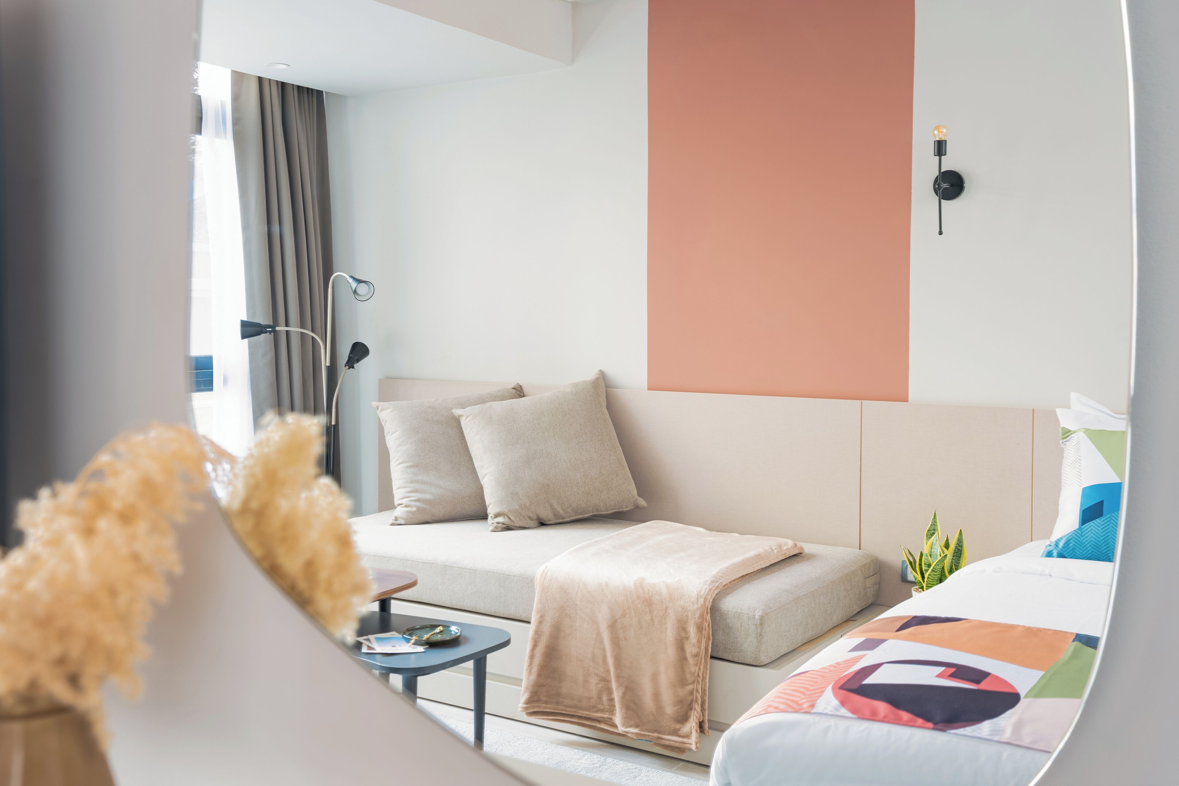 Ett modernt hotellrum med en soffa, en säng, ett litet bord och en krukväxt.