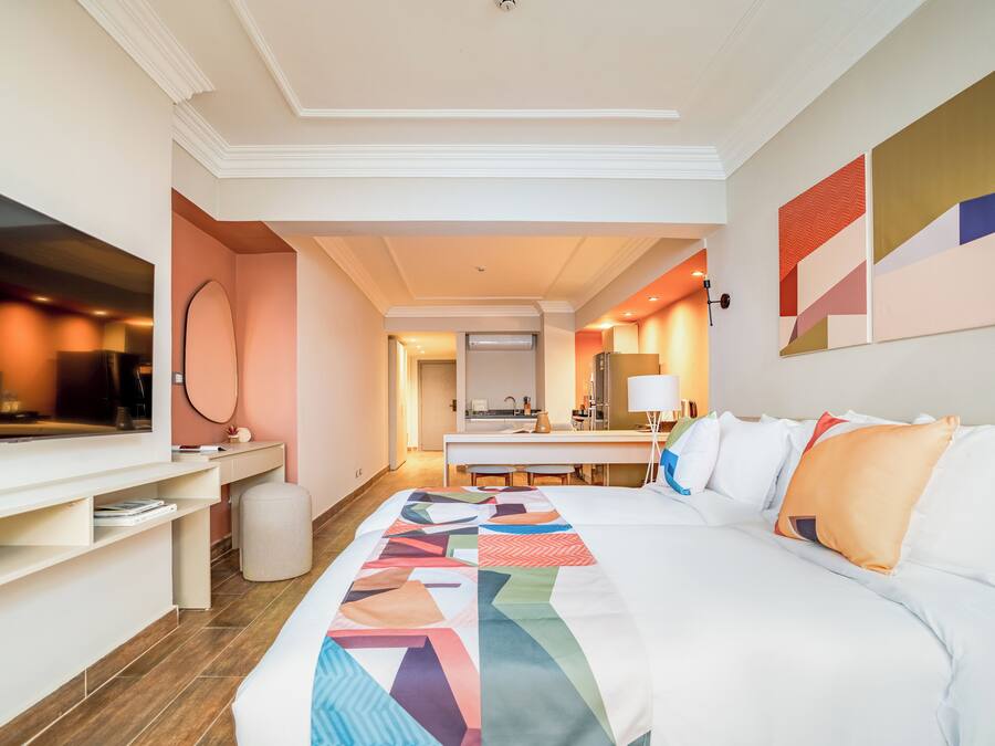 A hotel room with a bed, a desk, a TV, and a bathroom visible through an open door.