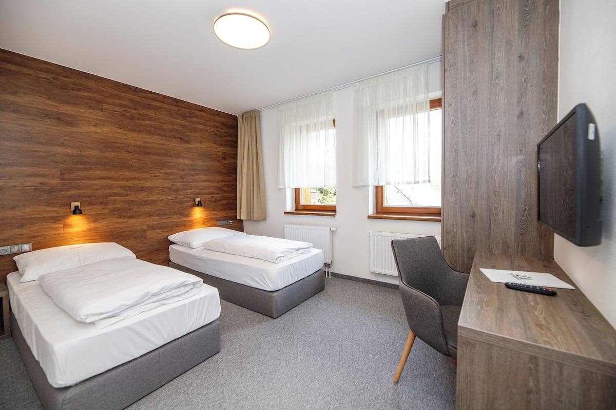 A hotel room with two beds, a desk with a chair, a TV, and a window with curtains.