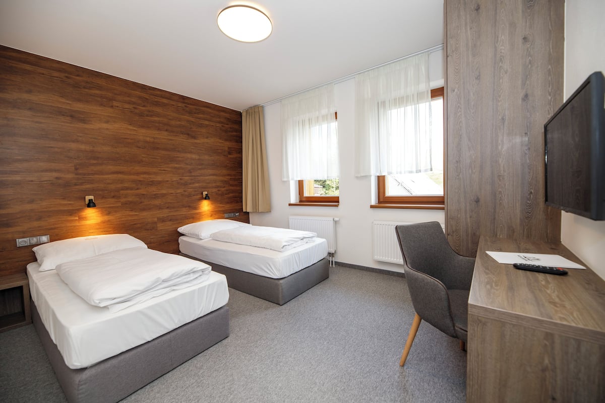 A hotel room with two beds, a desk, a TV, and a window with curtains.