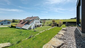 Une maison avec un toit en pente, une véranda couverte et un chemin de pierre menant à une terrasse en bois.