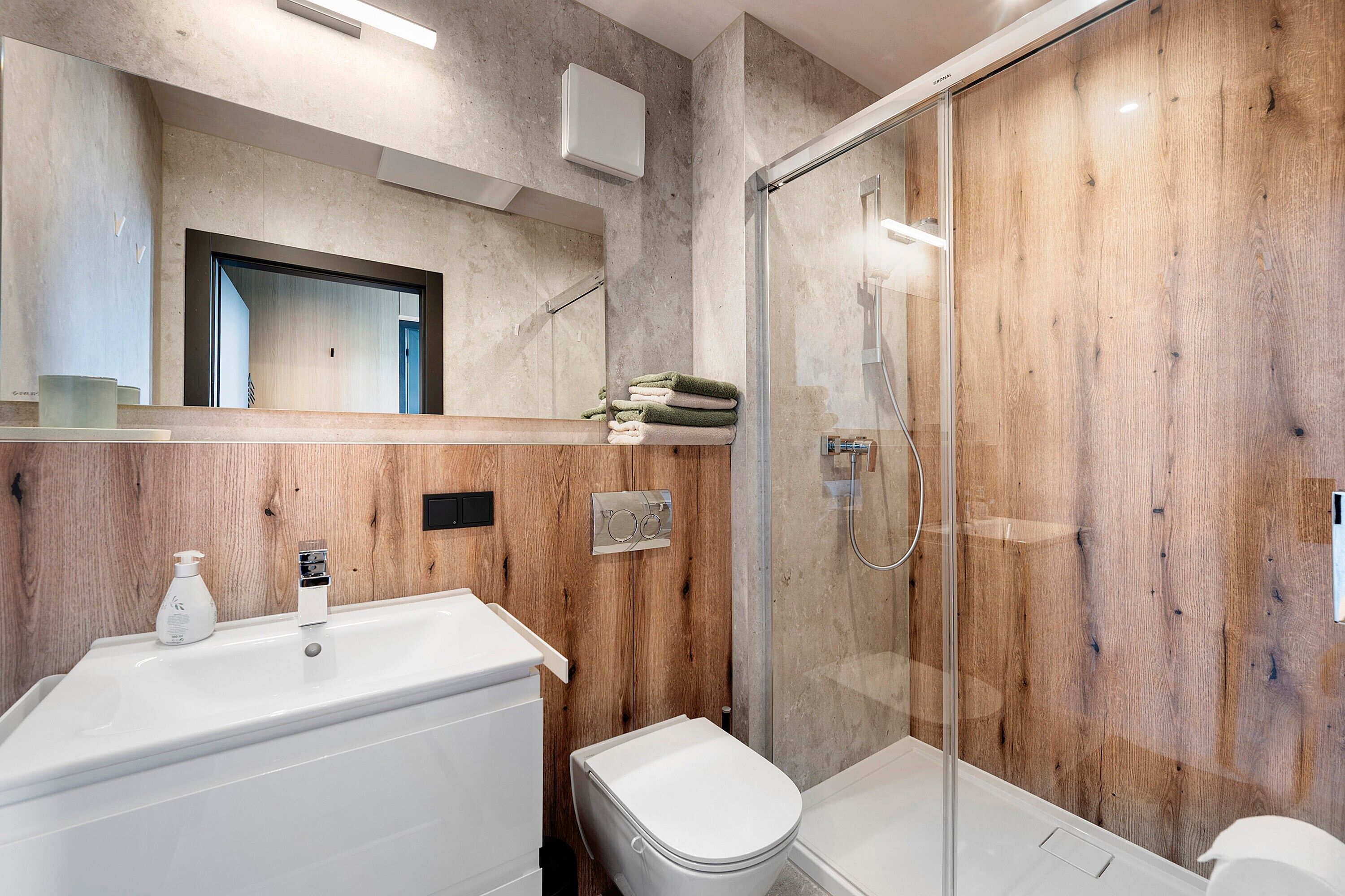 Een moderne badkamer met een houten wastafelmeubel, een douchecabine van glas en een wit toilet.