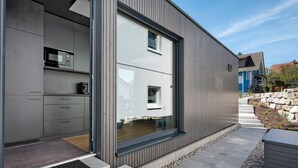 A modern exterior with a large sliding glass door, a metal staircase, and a stone wall. - Tiny Home 'Seewald - Tiny House' with Private Terrace, Shared Garden and Wi-Fi (Seewald)