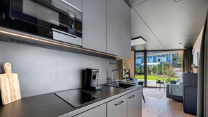 A modern kitchen with a built-in microwave, coffee maker, and a large window overlooking a blue house. - Tiny Home 'Seewald - Tiny House' with Private Terrace, Shared Garden and Wi-Fi (Seewald)