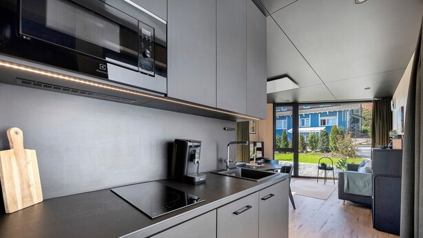 Een moderne keuken met een ingebouwde magnetron, koffiezetapparaat en een groot raam met uitzicht op een blauw huis.