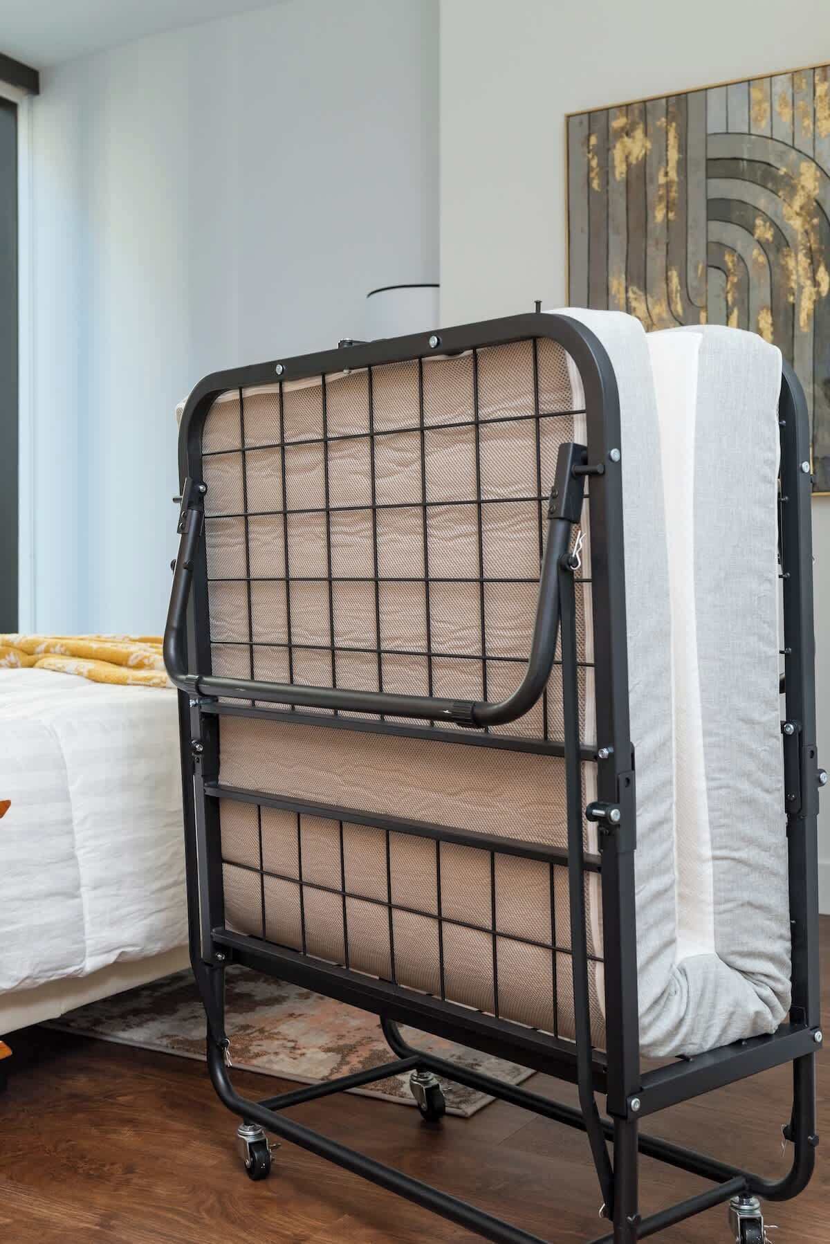 Una cama litera con estructura metálica y paneles de malla, ubicada en una habitación con una cama y un cuadro abstracto grande en la pared.