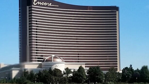 Un grand hôtel moderne à la façade caractérisée par des lignes horizontales, une structure en forme de dôme à l’avant et une étendue d’eau au premier plan.