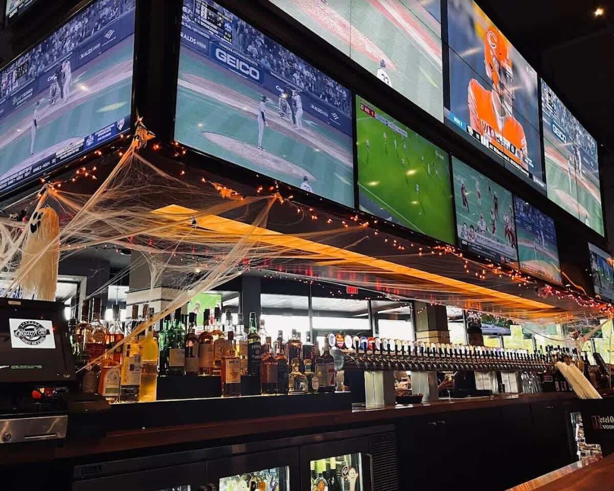 Zona de bar con varias pantallas mostrando eventos deportivos, una variedad de botellas de licor y una barra.