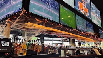 Zona de bar con varias pantallas mostrando eventos deportivos, una variedad de botellas de licor y una barra.