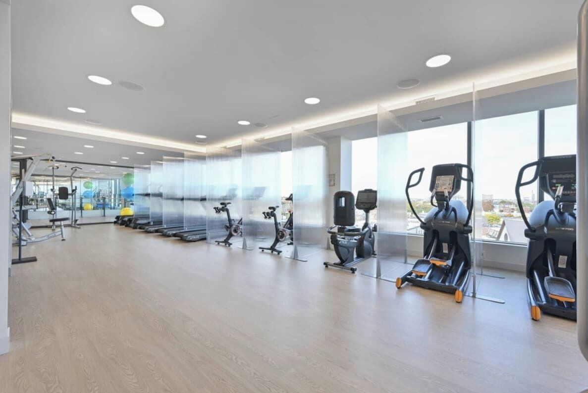 Un gimnasio moderno con máquinas de cardio, equipo de pesas y grandes ventanales con vistas a la ciudad.