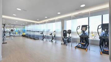 Un gimnasio moderno con máquinas de cardio, equipo de pesas y grandes ventanales con vistas a la ciudad.