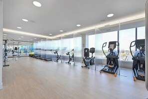 Une salle de sport moderne équipée de machines de cardio, d’appareils de musculation et de grandes fenêtres offrant une vue sur la ville.