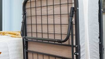Una cama litera con estructura metálica y paneles de malla, ubicada en una habitación con una cama y un cuadro abstracto grande en la pared.
