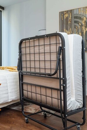Un lit superposé avec une structure en métal et des panneaux en treillis, placé dans une pièce qui contient également un lit et un grand tableau abstrait accroché au mur.