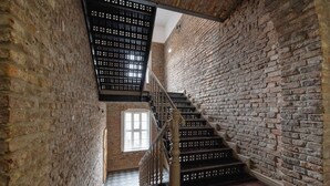 A staircase with a wooden handrail and black balusters, leading to a room with a brick wall and a window. - Functional Studio | Air Conditioning | Close to Train Station (Katowice)