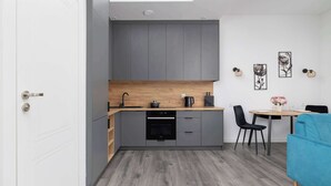 A modern kitchen with grey cabinets, a wooden countertop, and a built-in oven. There is a dining area with a table and chairs, and a blue sofa. - Functional Studio | Air Conditioning | Close to Train Station (Katowice)