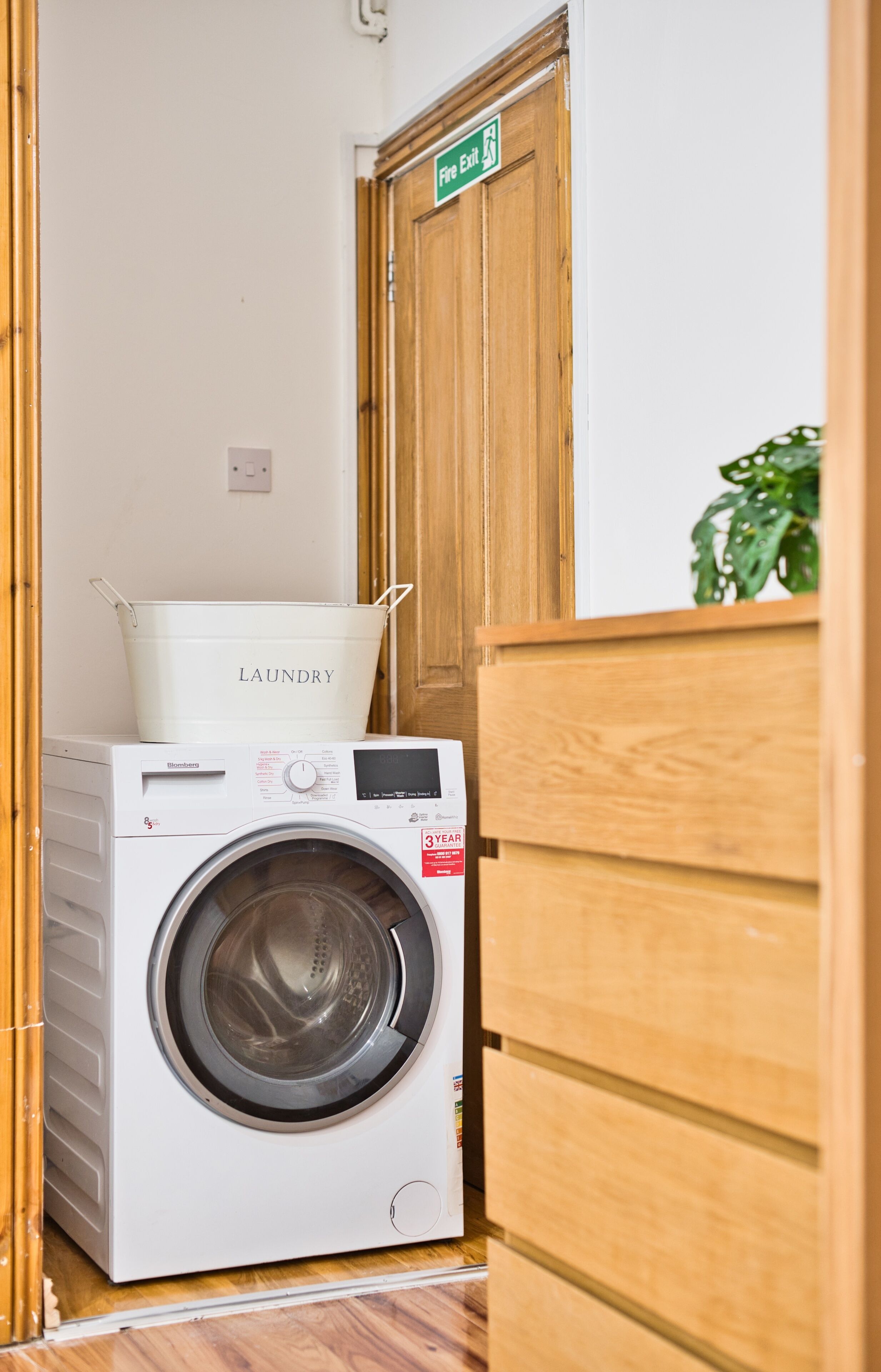 A compact laundry area with a washing machine and a laundry basket labeled "LAUNDRY" on a wooden cabinet.