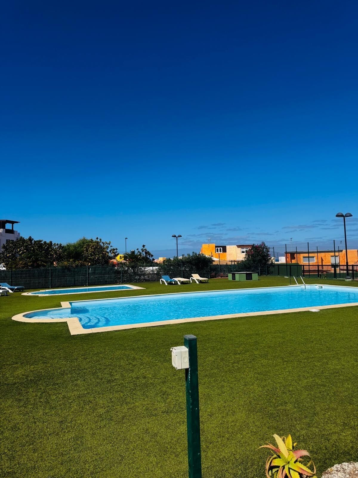 Una piscina amb una tanca verda, una torre de socorrista i gandules.