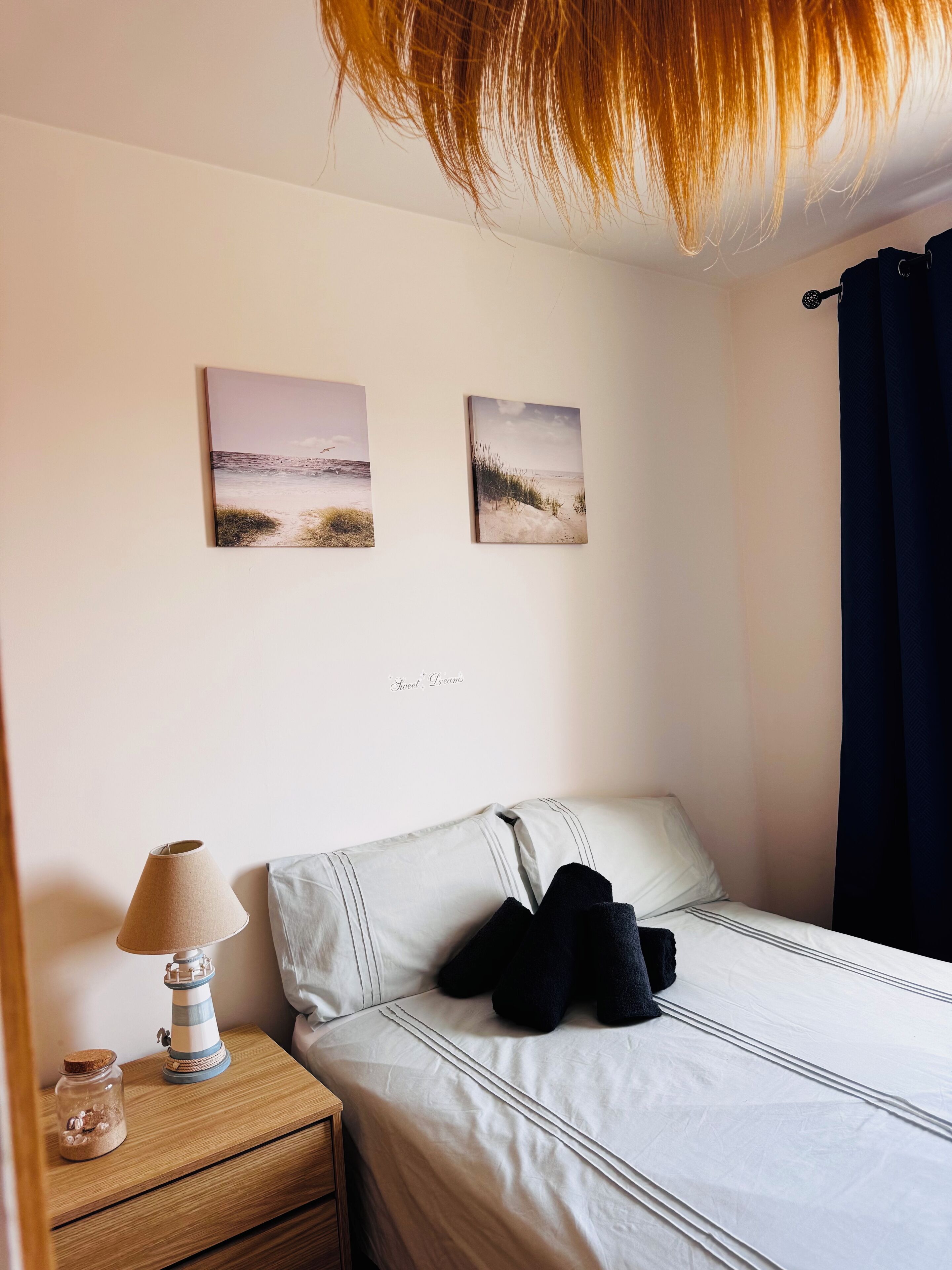 Une chambre à coucher avec un lit, une table de chevet avec une lampe et deux tableaux accrochés au mur.