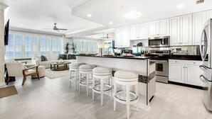Una cucina moderna con mobili bianchi, elettrodomestici in acciaio inossidabile e un angolo bar con sgabelli.