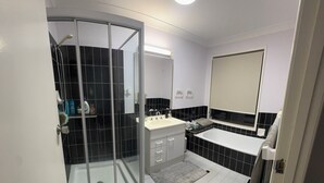 A modern bathroom with a glass shower enclosure, a sink, and a large mirror. - Quiet cozy room by the beach R1 (Brighton)