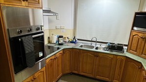A kitchen with wooden cabinets, a stainless steel refrigerator, an oven, a sink, and a window above the sink. - Quiet cozy room by the beach R1 (Brighton)