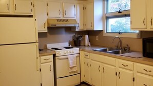 A compact kitchen with white cabinets, a stove, a refrigerator, and a window.