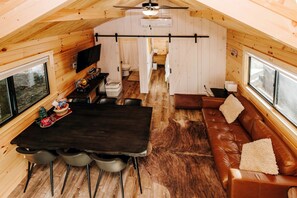 Ein gemütliches Blockhaus-Interieur mit Esstisch, Stühlen, einer Ledersofa und einem Fernseher.