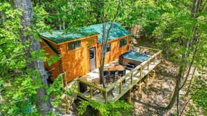A wooden cabin with a hot tub, deck, and surrounded by trees.