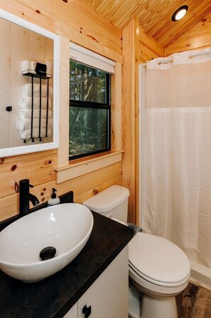 A wooden cabin bathroom with a white sink, toilet, and shower curtain.