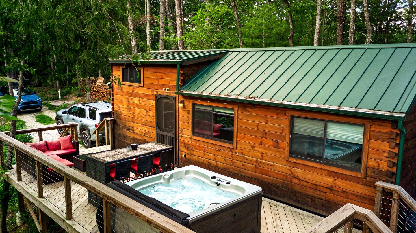 A wooden cabin with a hot tub, deck, and a covered outdoor seating area.