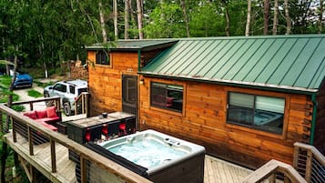 A wooden cabin with a hot tub, deck, and a covered outdoor seating area.
